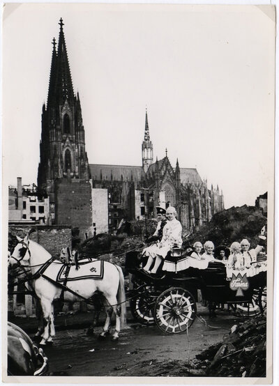 Karnevalisten in einer Kutsche, im Hintergrund ist der Kölner Dom zu sehen