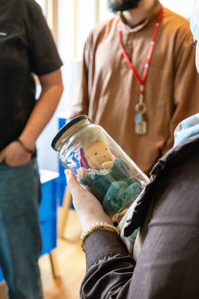 Frau hält ein Glas mit einer Stoffpuppe darin in Händen.