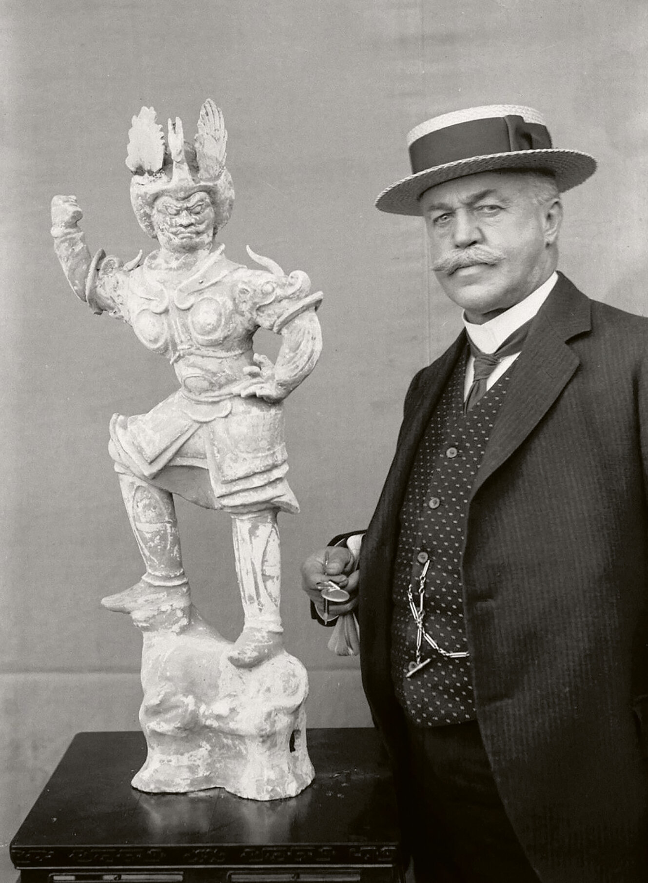 Foto von Adolf Fischer, mit Hut neben einer Statue stehend.