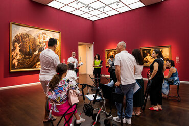 Eine Gruppe von Menschen steht im Museumsraum und hört dem Guide zu.