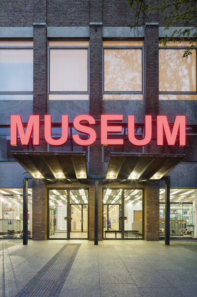 Glass doors at the entrance to the MAKK, with illuminated lettering above them reading Museum