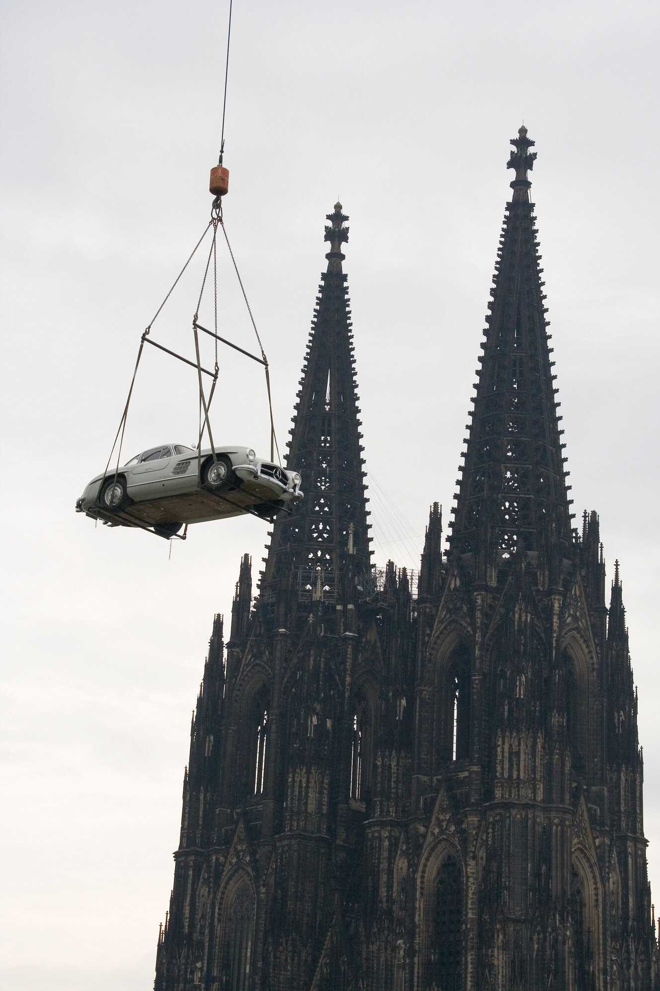 Ein Mercedes-Auto an einem Kran, im Hintergrund der Kölner Dom