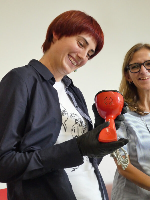 Annalena Knors (links) und Kuratorin Romana Rebbelmund mit dem »Ericofon« von 1954: Das frühe Kunststofftelefon verbirgt Wählscheibe und Auflege-Knopf unter seinem Fuß.