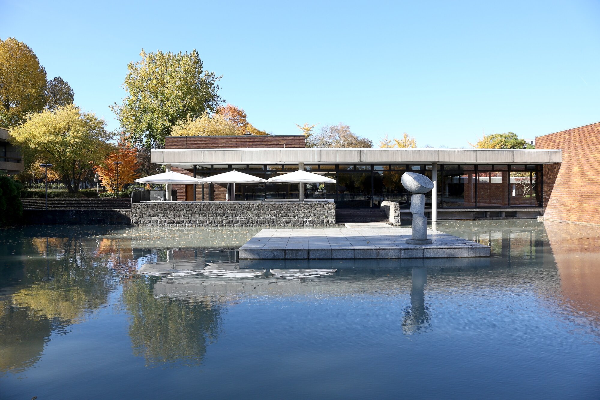 Vor einem flachen Bungalow erstreckt sich eine Terrasse mit Sonnenschirnen und ein Gartenteich