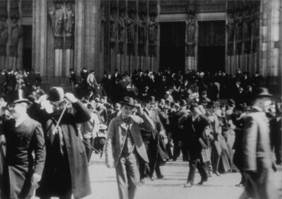 Historische Schwarz-Weiß-Aufnahme einer Menschenmenge, die den Kölner Dom nach dem Gottesdienst verlässt. Frauen in langen Kleidern und Männer in dunkler Kleidung gehen über den Vorplatz.
