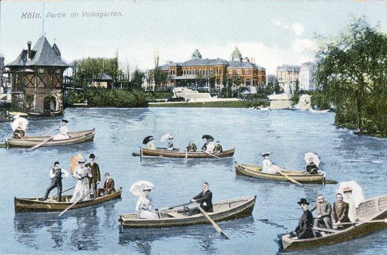 Historische Fotografie zeigt Personen in mehreren Ruderboote auf einem See. Im Hintergrund befinden sich Gebäude.