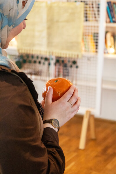 Frau hält eine kleine Skulptur in Form einer Orange.