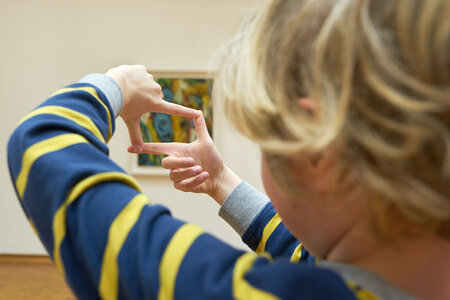 Ein Kind betrachtet ein Gemälde durch seine zum Quadrat geformten Finger. 