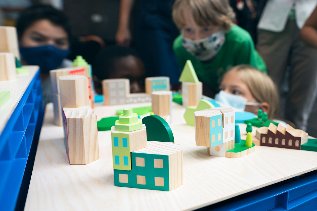Kinder schauen gemeinsam auf eine aus Bauklötzen gebaute Szene