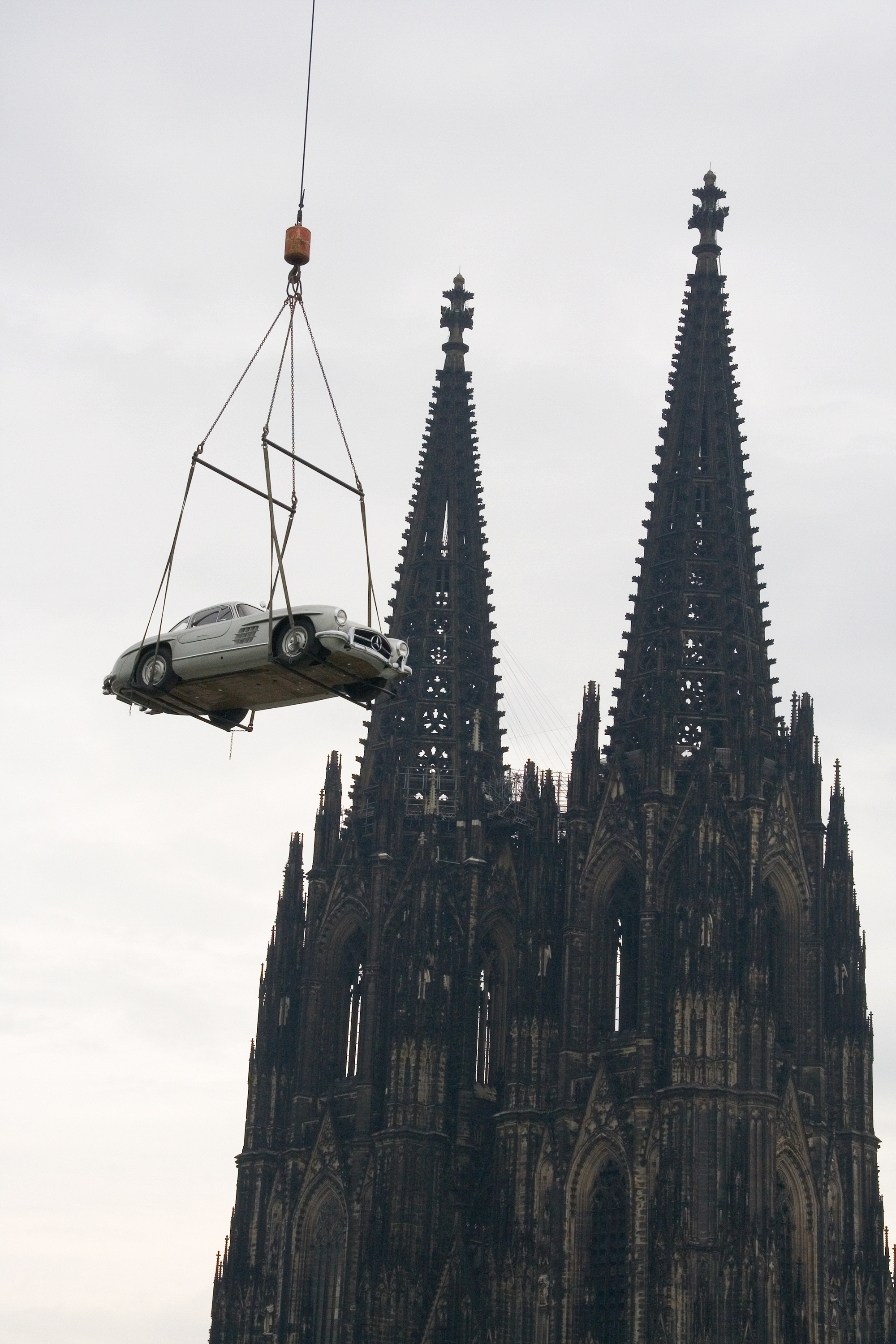Ein Mercedes-Auto an einem Kran, im Hintergrund der Kölner Dom