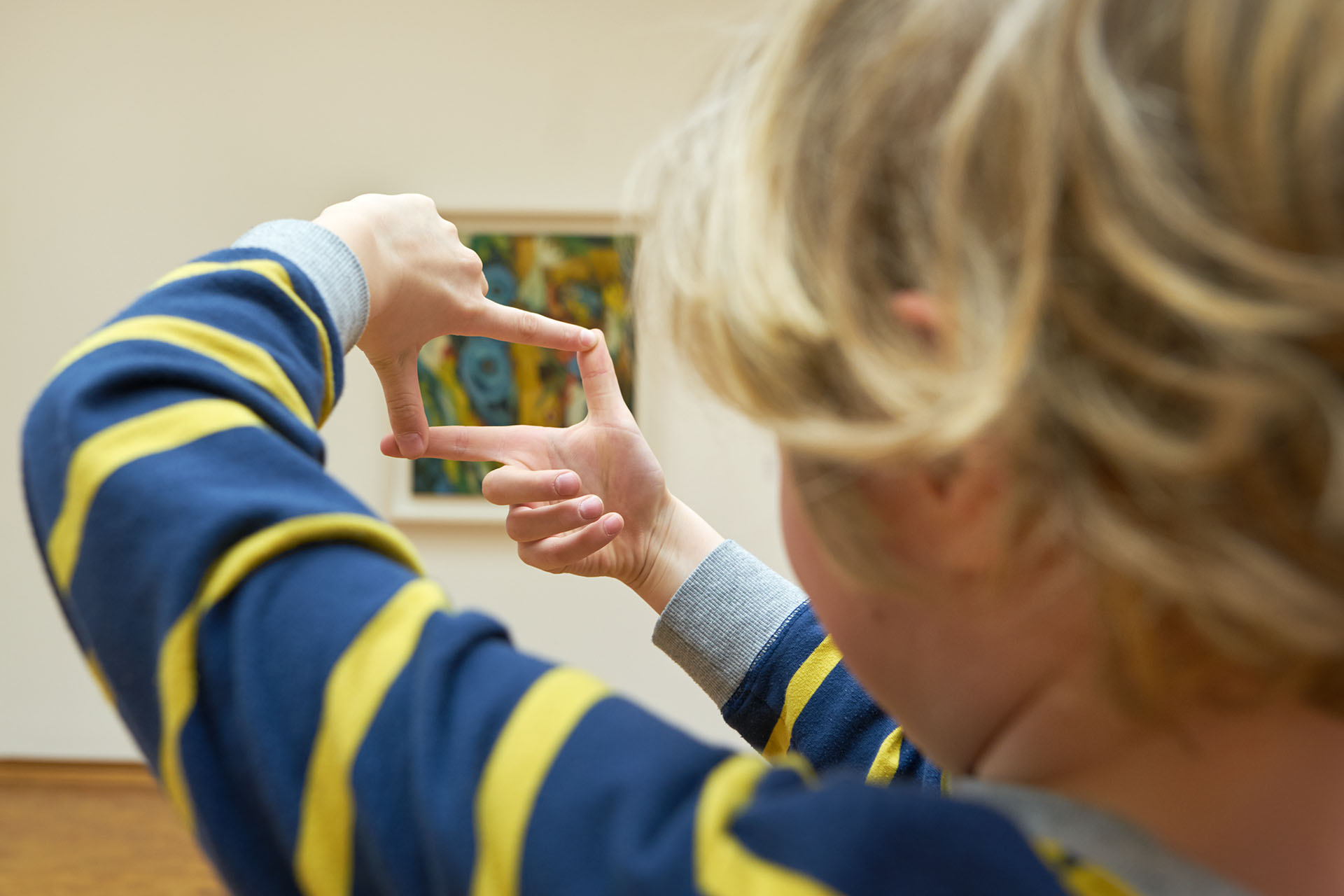 Ein Kind betrachtet ein Gemälde durch seine zum Quadrat geformten Finger. 
